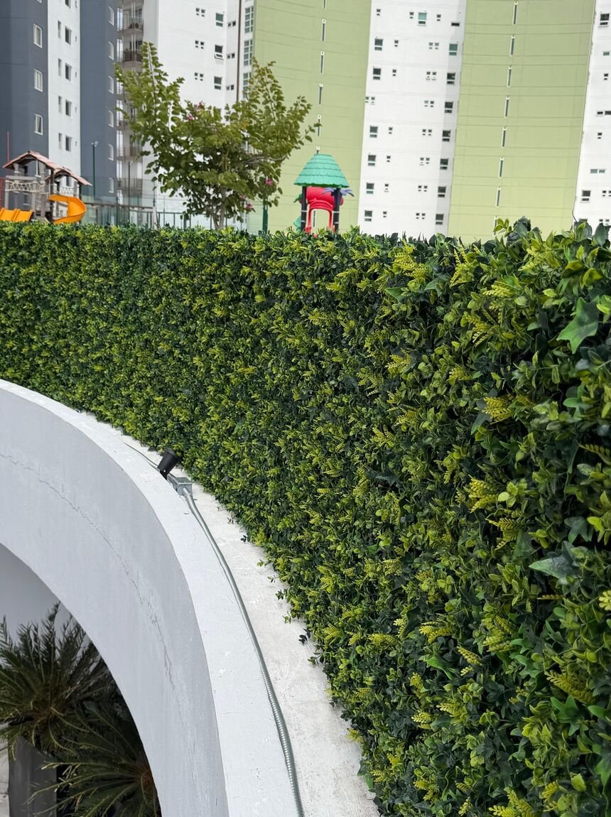 Muro verde de follaje artificial instalado por Game Turf sobre un muro curvo, con torres residenciales detrás.