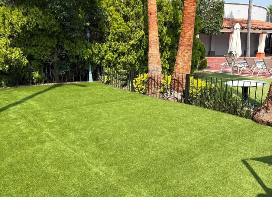 Área ajardinada con pasto sintético Game Turf en un conjunto residencial, delimitada con reja y vegetación.
