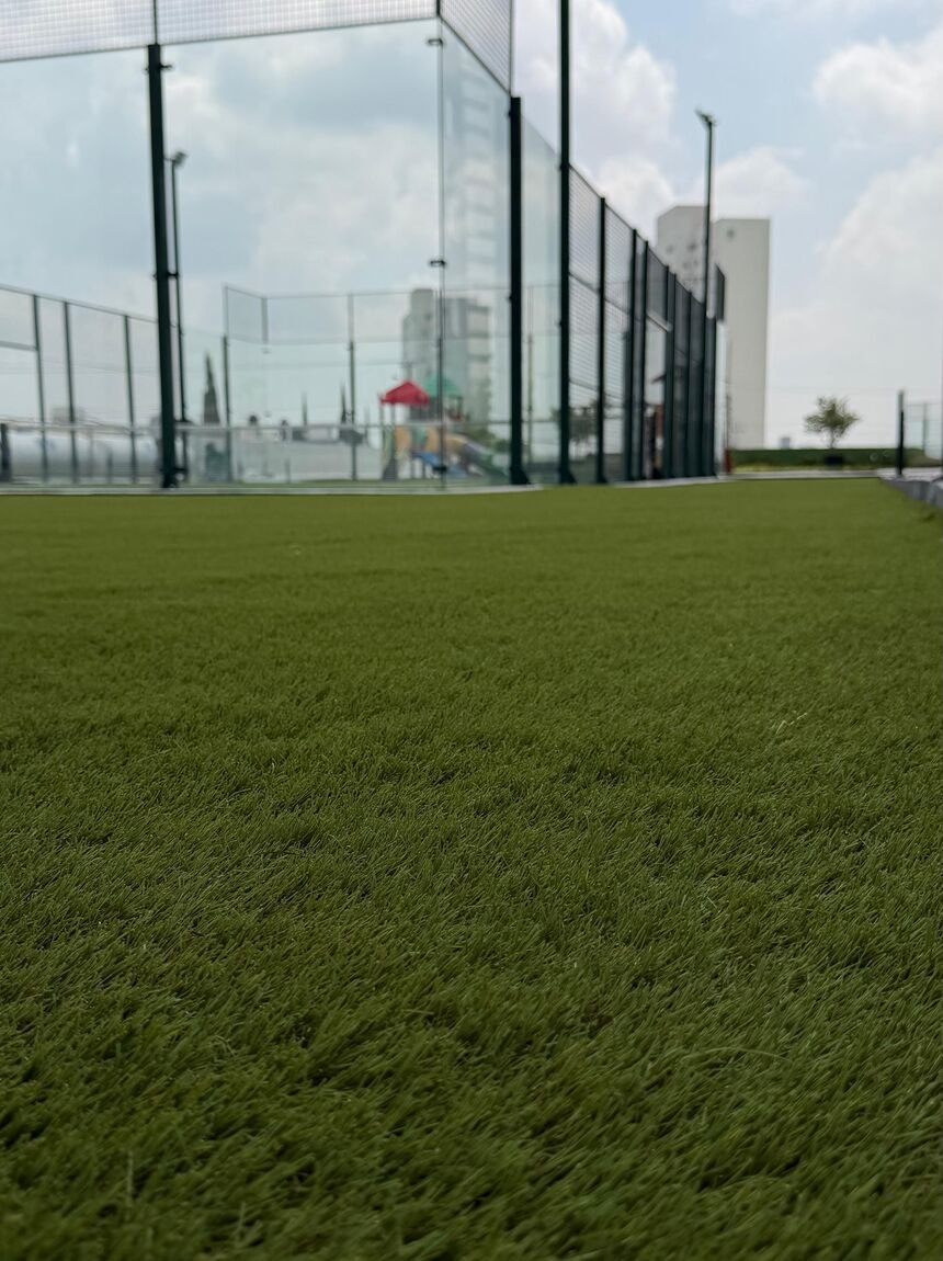 Área común de un conjunto residencial con pasto sintético Game Turf, cancha techada y juegos infantiles al fondo.
