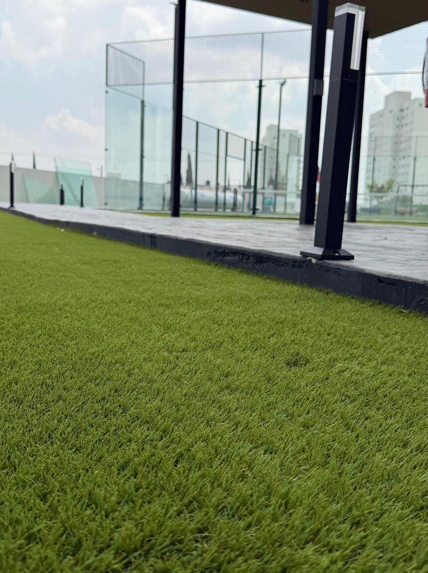 Pasto sintético Game Turf en el perímetro de una cancha de pádel de cristal dentro de un desarrollo residencial.